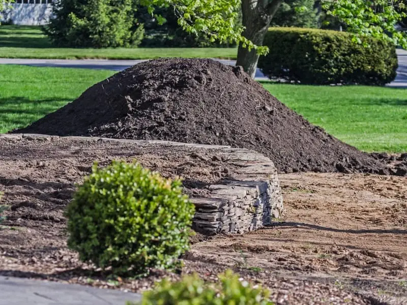 Large mound of dark topsoil beside stone garden wall