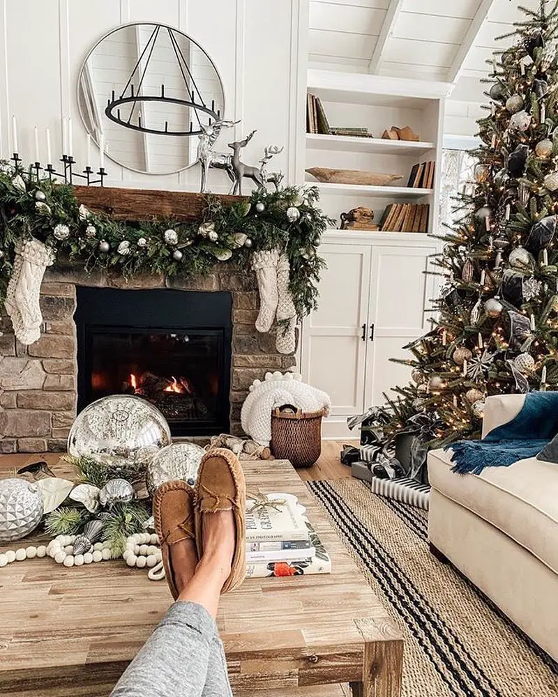 Festive living room with lit fireplace, Christmas tree, and person's feet in view.