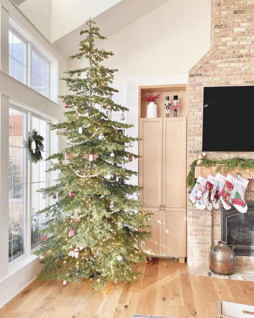 Beautifully decorated Christmas tree in living room with brick fireplace and stockings.