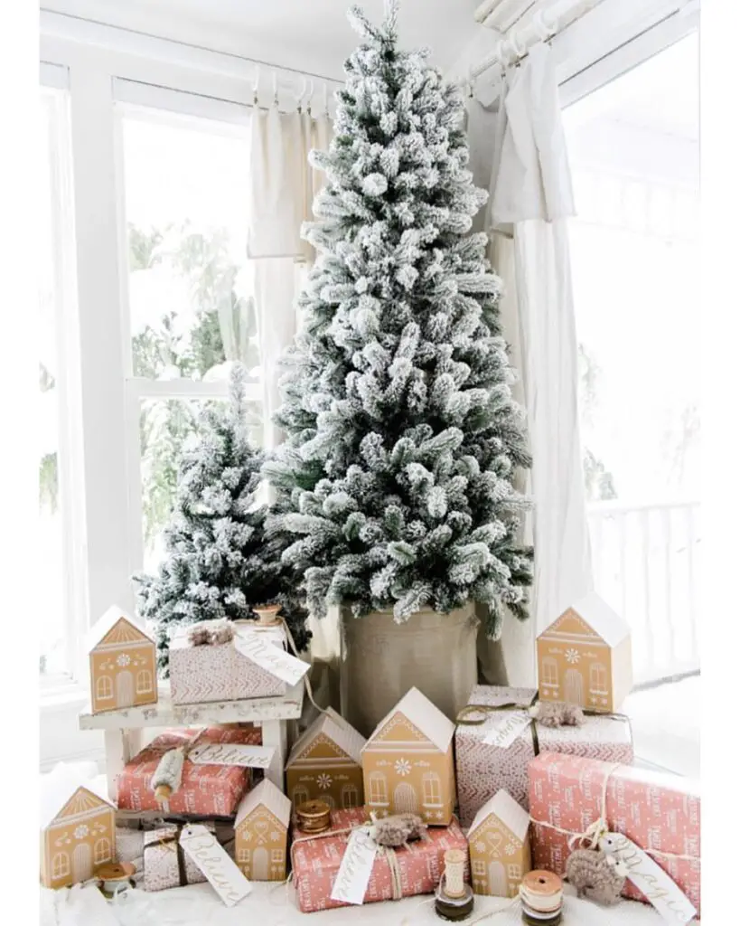 A snowy Christmas tree surrounded by wrapped presents and decorative houses.