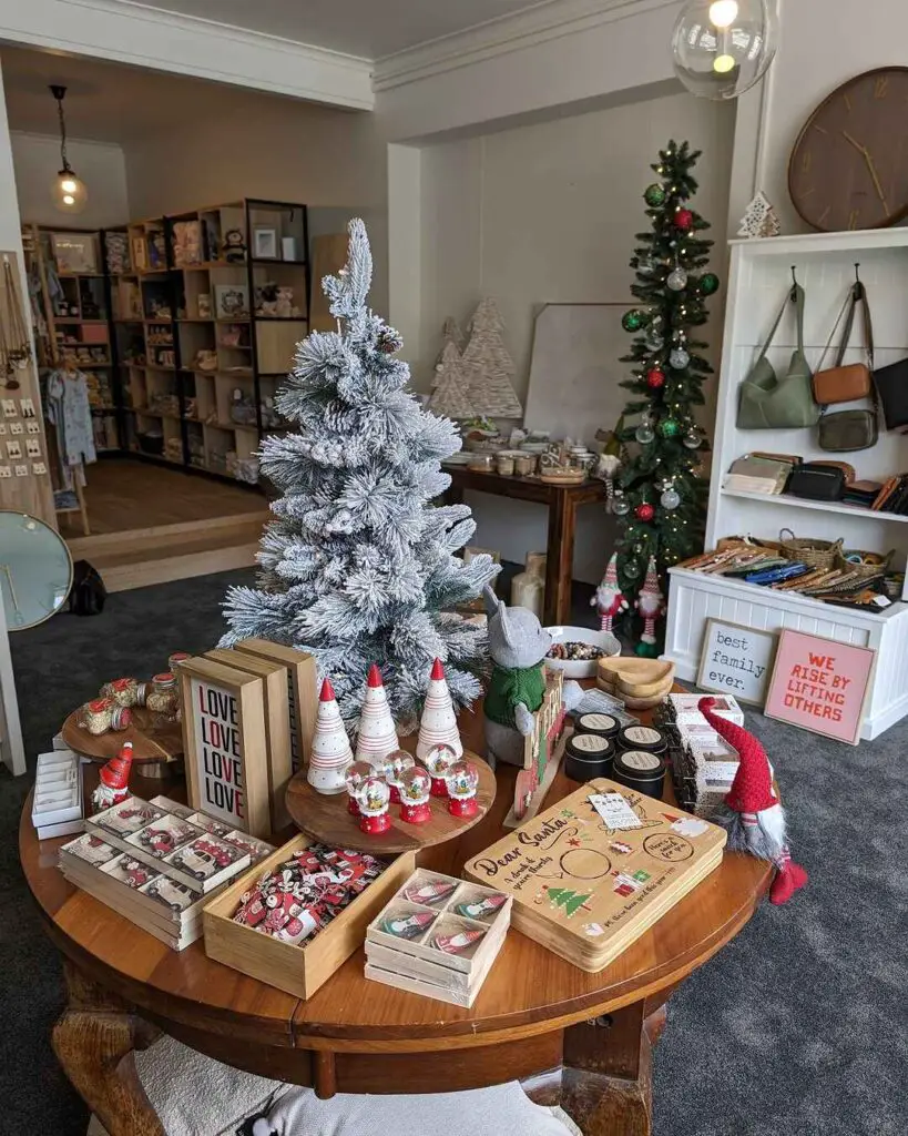 Festive boutique display with flocked tree, Christmas decorations, and gift items on wooden table