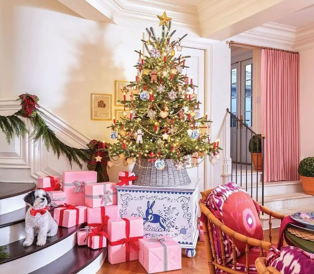 A living room with an ornately decorated Christmas tree surrounded by pink gifts, cozy furniture