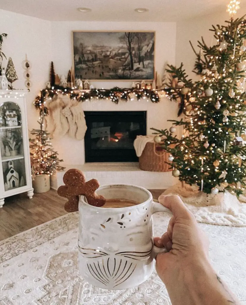 A festive living room setting with a lit fireplace, Christmas tree, and a hand holding a mug with a gingerbread cookie.