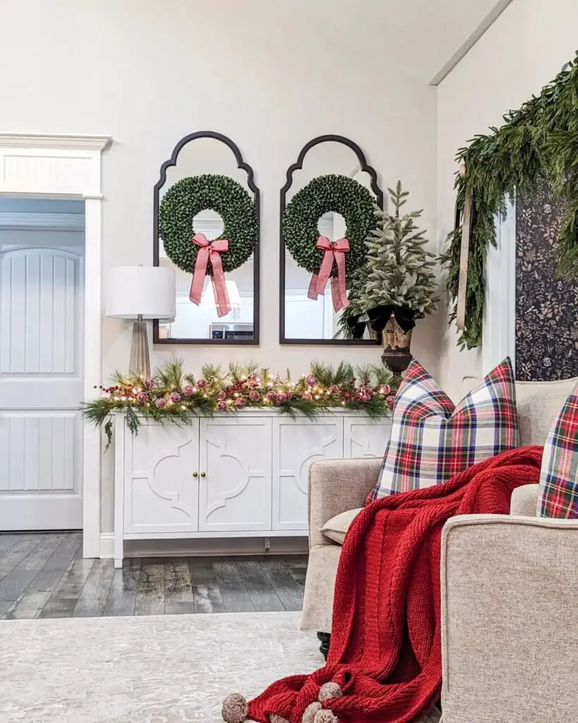 Living room with twin boxwood wreaths, floral garland, tartan sofa and cozy red throw capturing seasonal warmth.