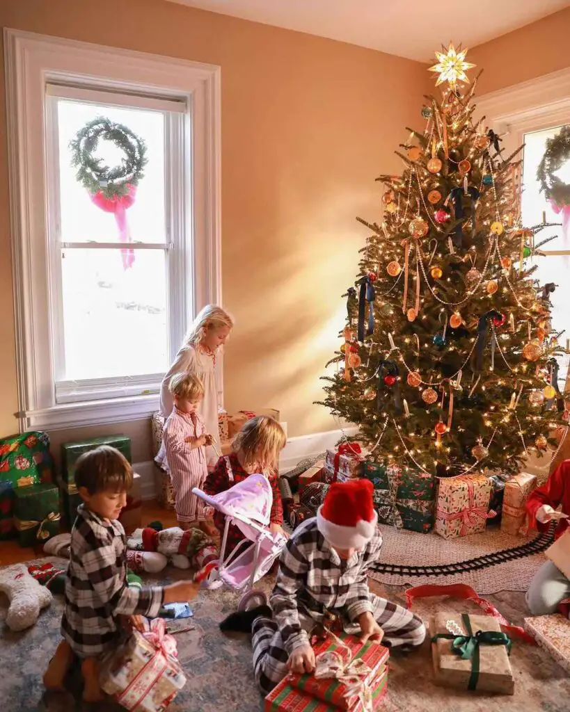 Children opening presents around Christmas tree in sunlit room