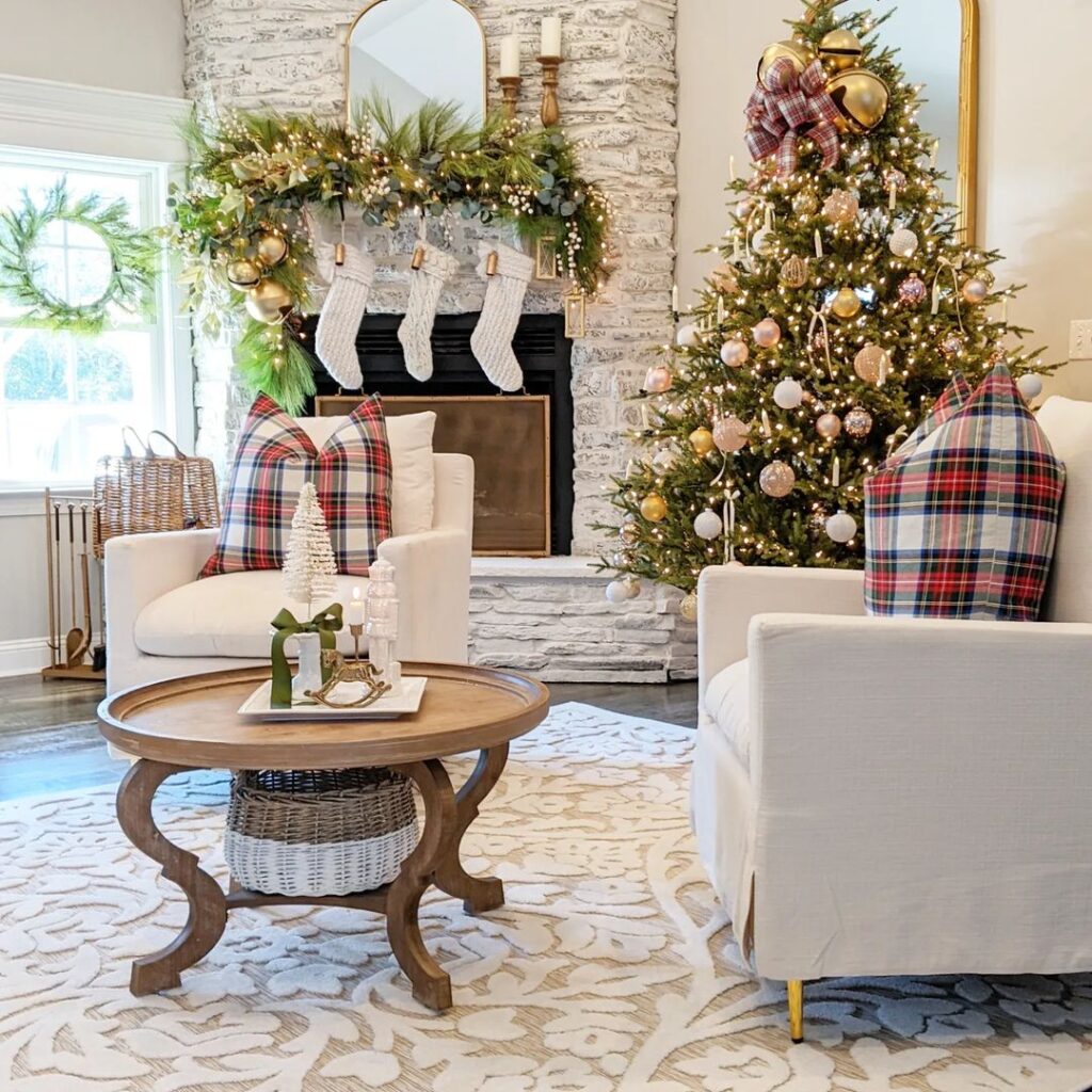 A cozy living room with stone fireplace, decorated Christmas tree, white sofas with plaid pillows and a rustic coffee table.