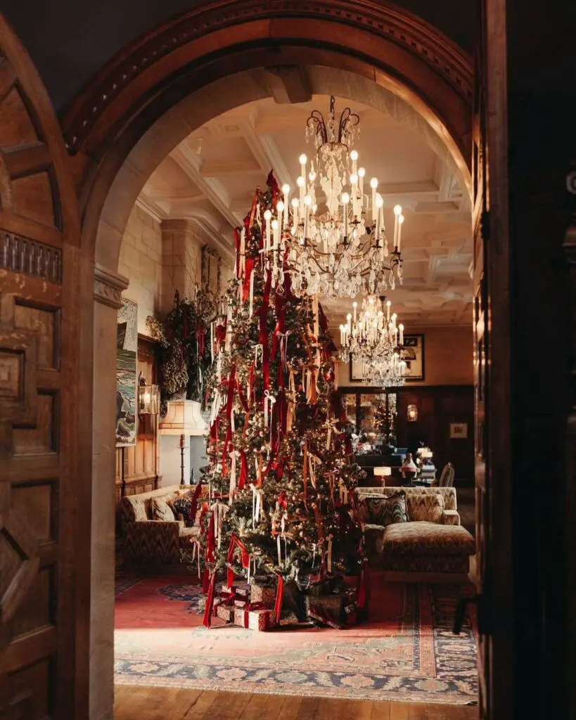 An ornately decorated Christmas tree with crimson ribbons stands beneath a grand archway