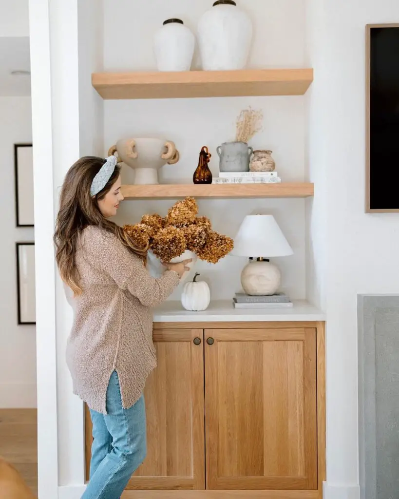 Woman arranging dried flowers on built-in shelves with fall decor