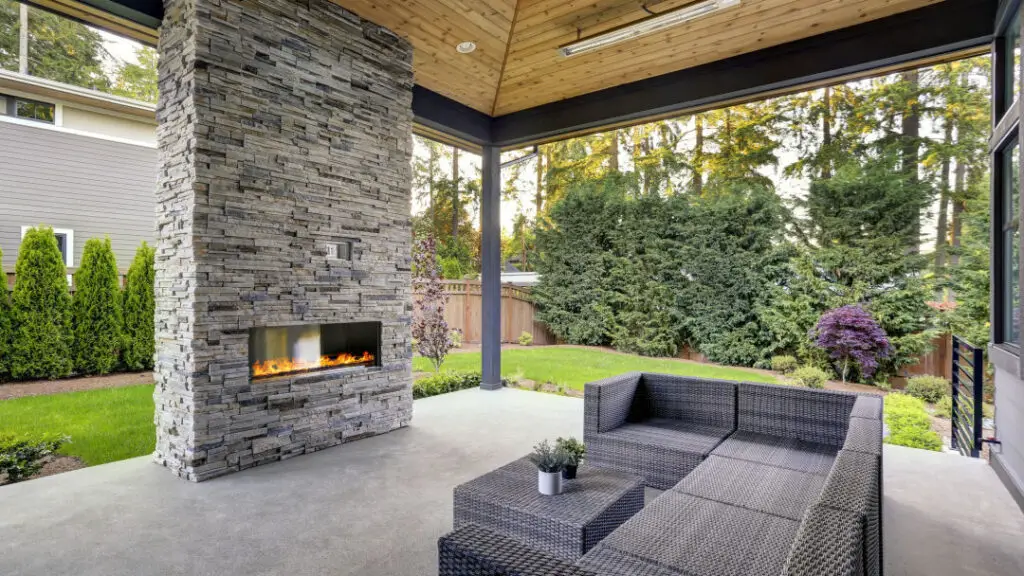 Covered patio with stone fireplace and wicker furniture surrounded by trees