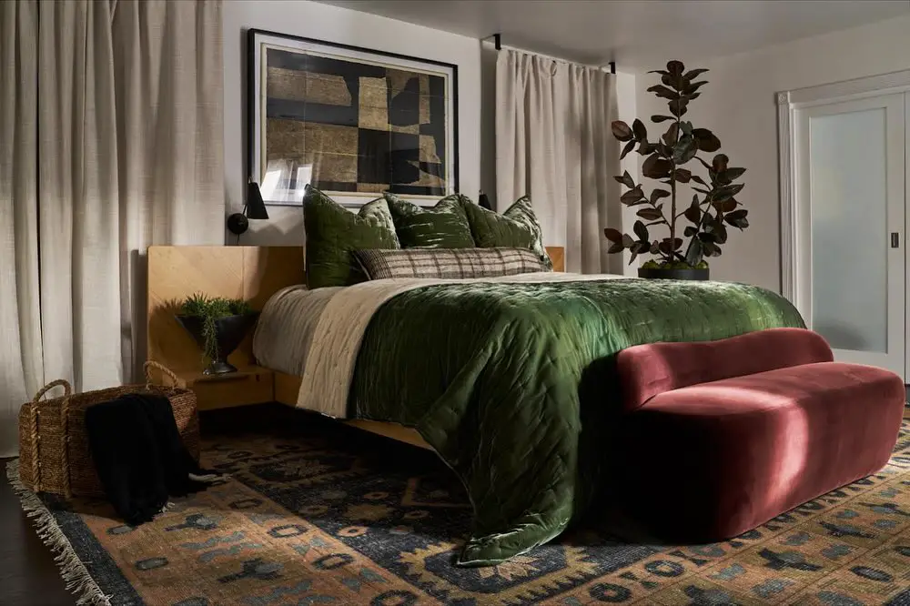 Bedroom with green bedding burgundy bench and abstract art