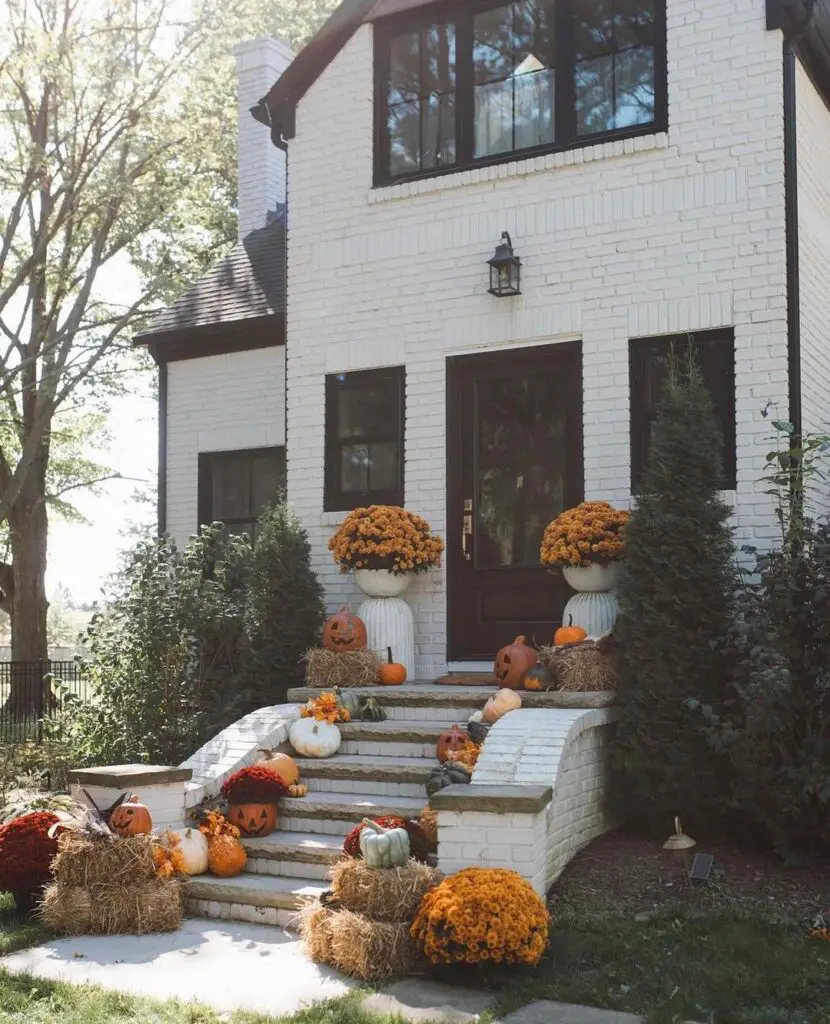 White brick house entrance decorated with pumpkins mums and hay bales