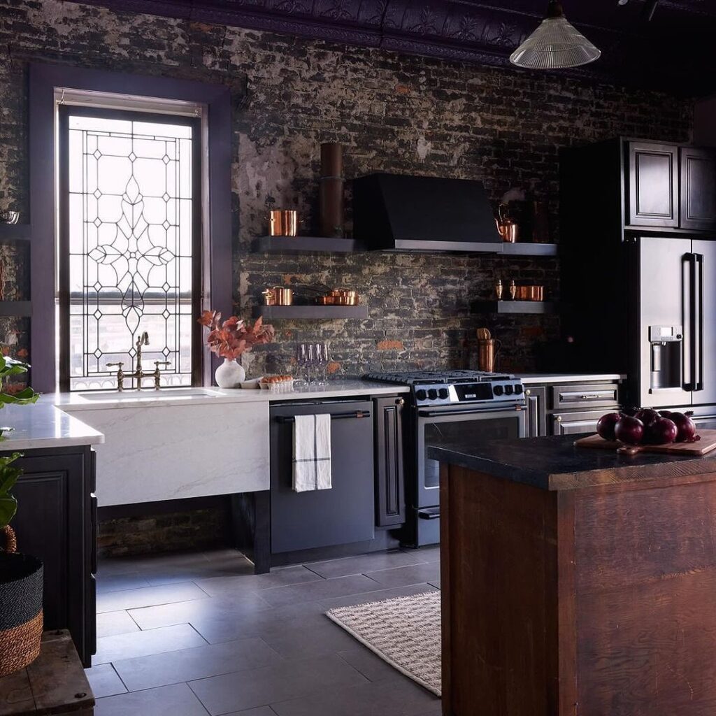 Rustic industrial kitchen with brick walls, wood island, and stone fireplace.