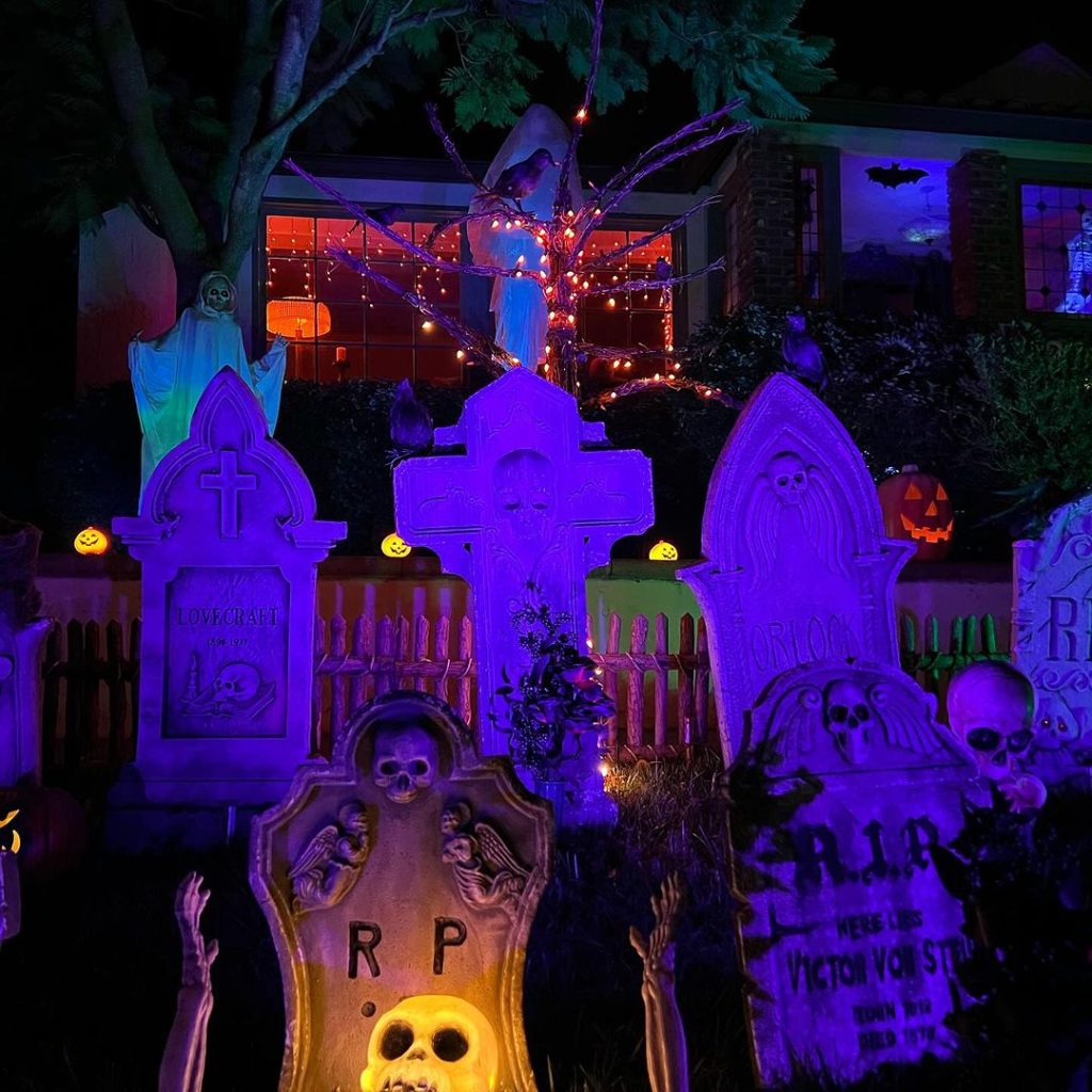 Purple-lit Halloween yard with tombstones ghost and glowing pumpkins
