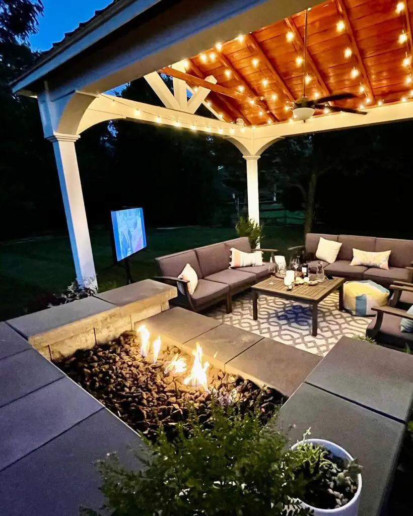 Illuminated pergola with cozy seating fire pit and outdoor TV at night