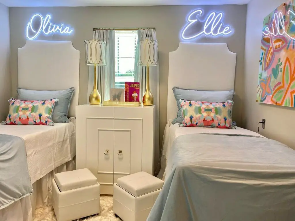Twin dorm beds with neon name signs and patterned pillows.