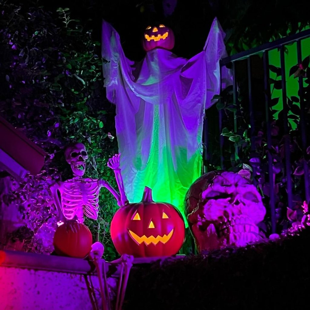 Colorfully lit Halloween scene with ghost skeleton and glowing pumpkins at night