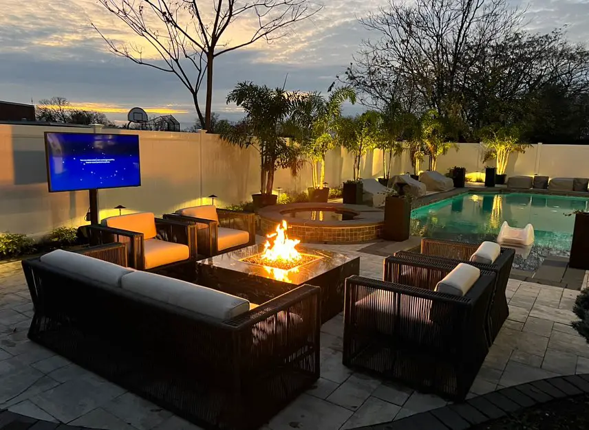 Backyard with fire pit seating outdoor TV and pool at sunset