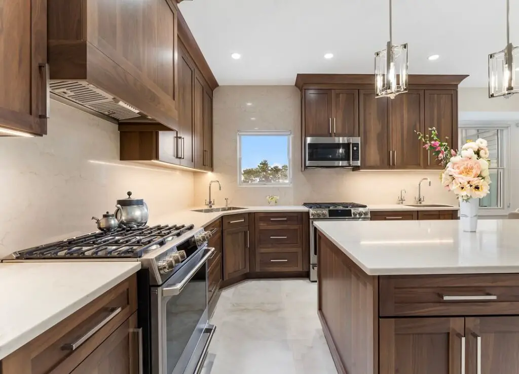 Warm-toned wood kitchen with island, pendant lights, floral vase.