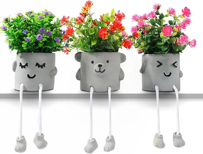 Three cute plant pots with faces and dangling rope legs are lined up on a shelf.
