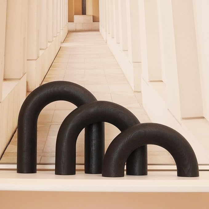 Three black, arch-shaped sculptures stand on a beige surface in front of a symmetrical hallway with tall, cream-colored columns