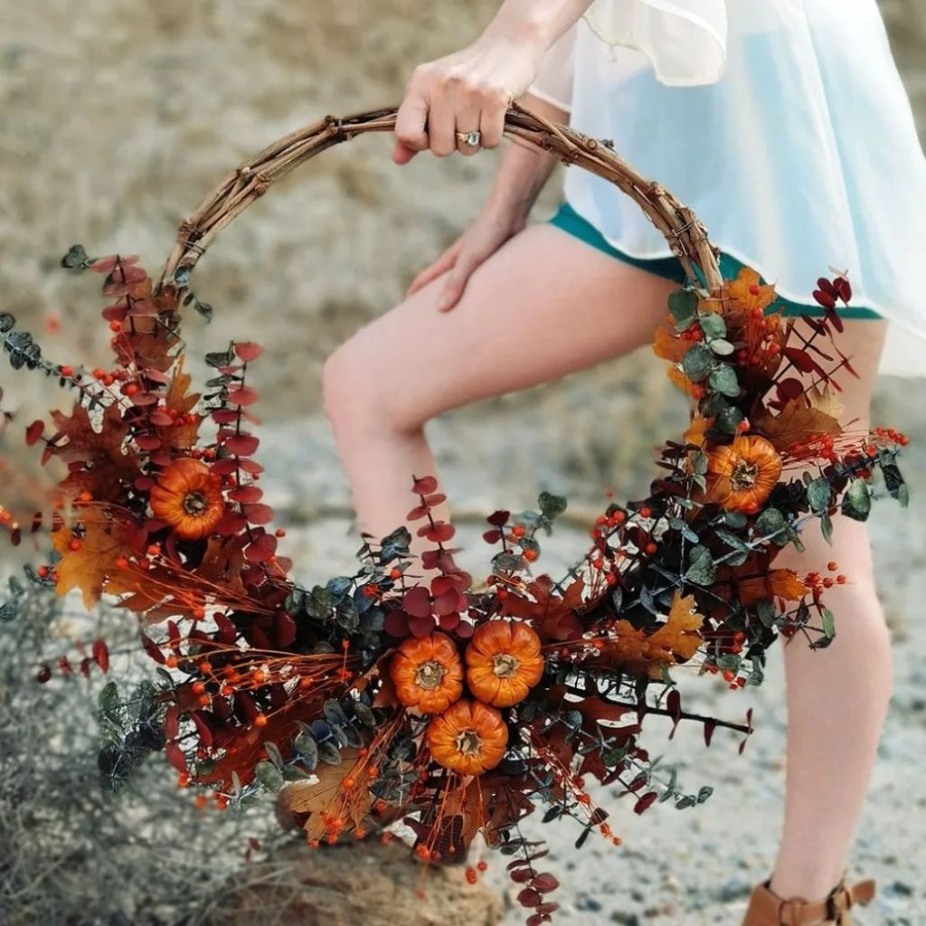 Hand holding fall wreath with pumpkins and colorful leaves