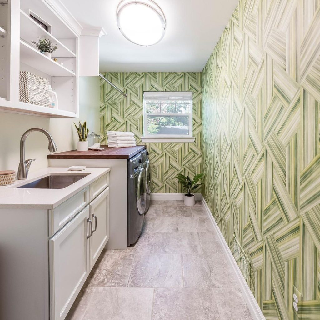 Laundry room with green geometric wallpaper and white cabinets.
