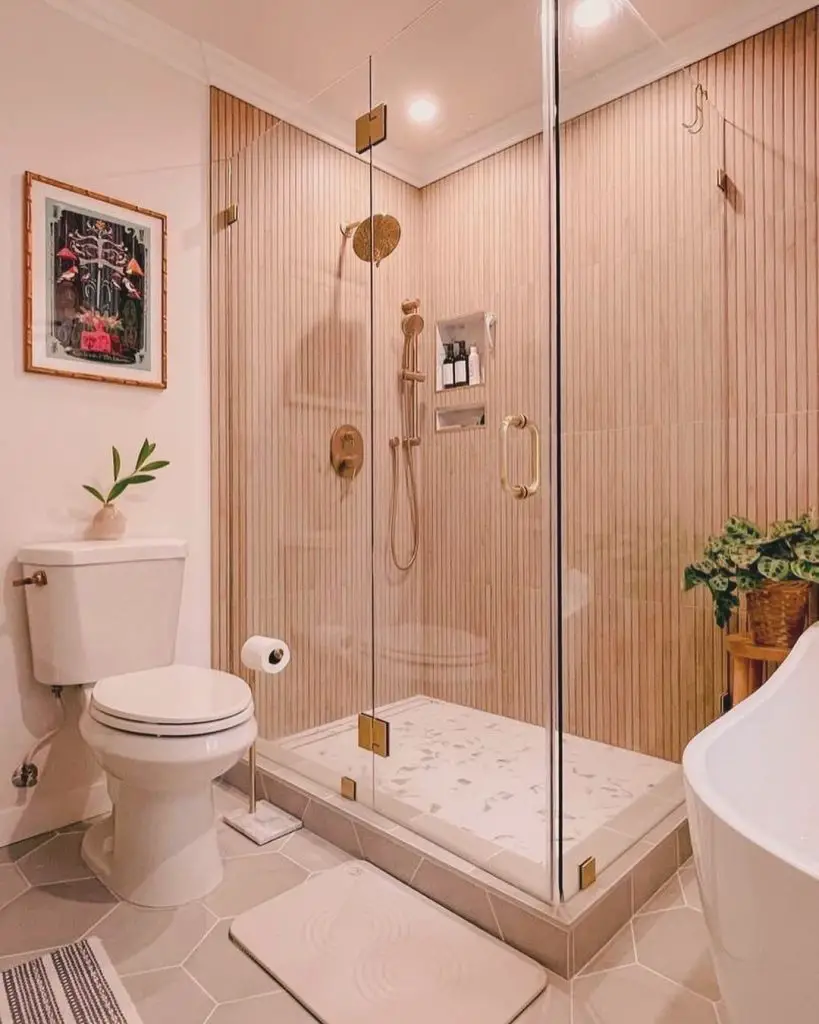 Pink bathroom with gold-trimmed glass shower and plants