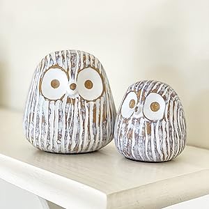 Two decorative owl figurines made of wood sit on a white surface. The larger owl is on the left, and the smaller owl is on the right.