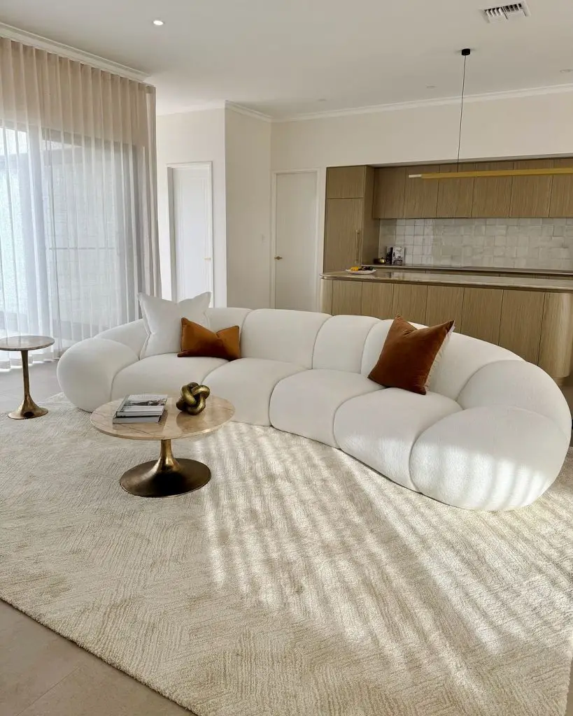 Curved white sofa with brown pillows in modern open-concept living room and kitchen.