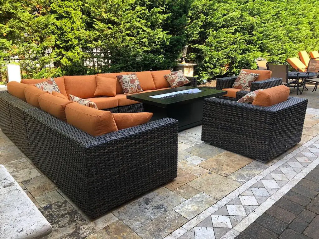 Outdoor patio with orange cushioned wicker furniture around fire table