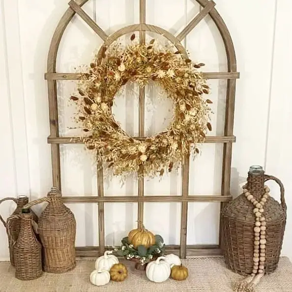 Golden grass wreath on wooden window frame with pumpkins and wicker jugs