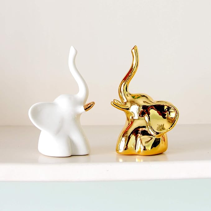 A white ceramic elephant figurine with its trunk up stands next to a shiny gold elephant figurine, also with its trunk raised.