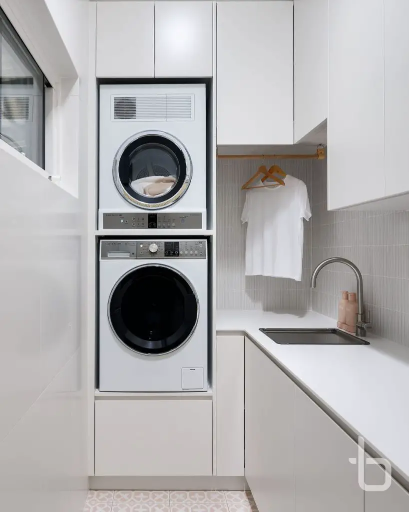 Compact white laundry room with stacked machines and hanging area