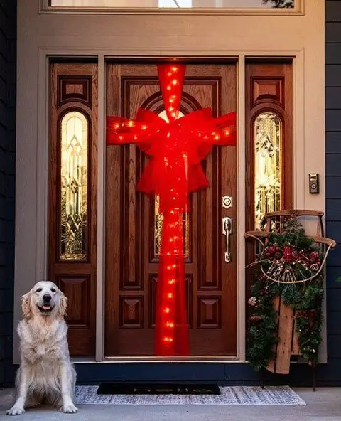 Dog sitting by door with large lit red bow decoration