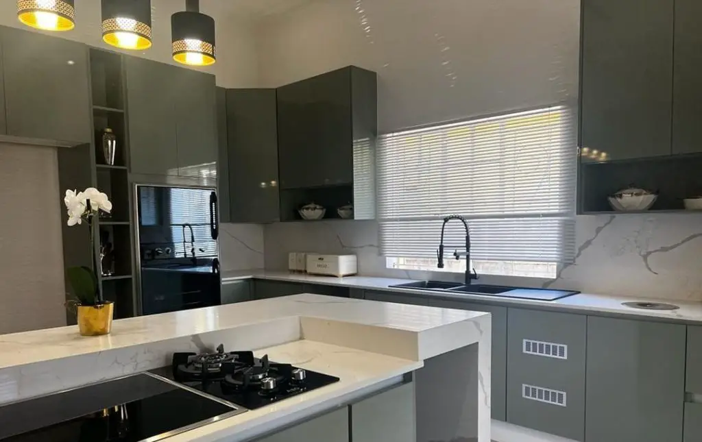 Modern sage green kitchen with marble countertops and pendant lights