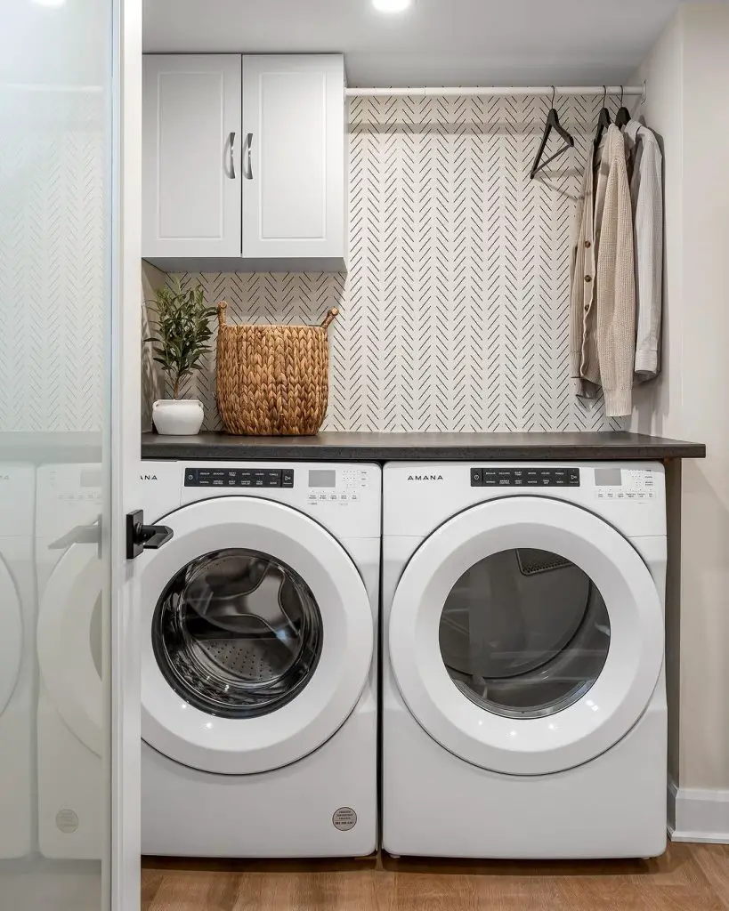 Compact laundry room with white appliances herringbone wallpaper and hanging space