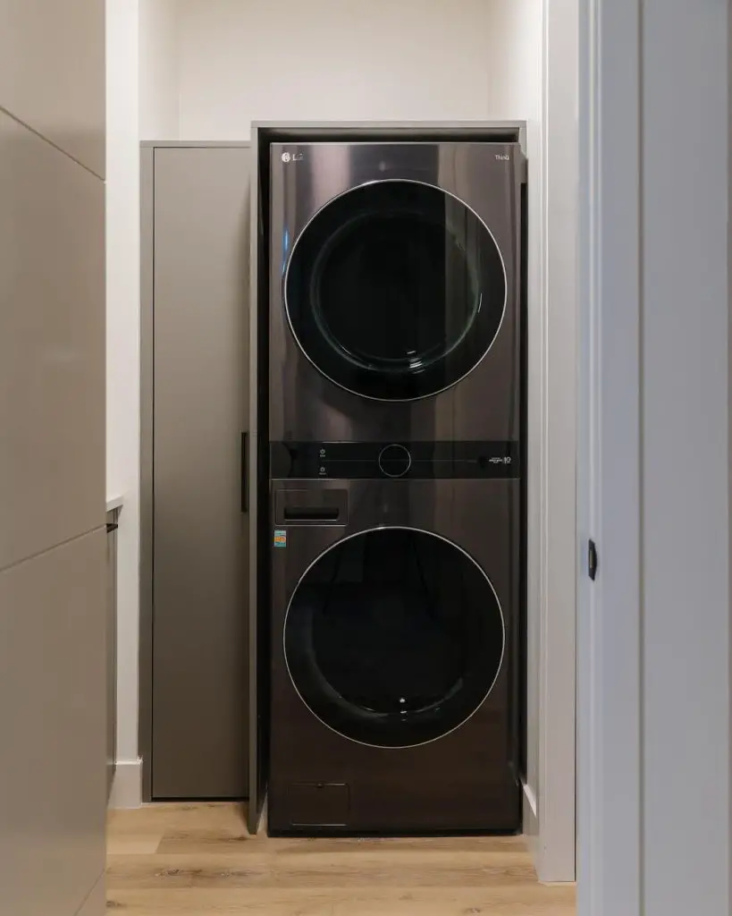 Stacked black LG washer-dryer in white alcove with wood floor