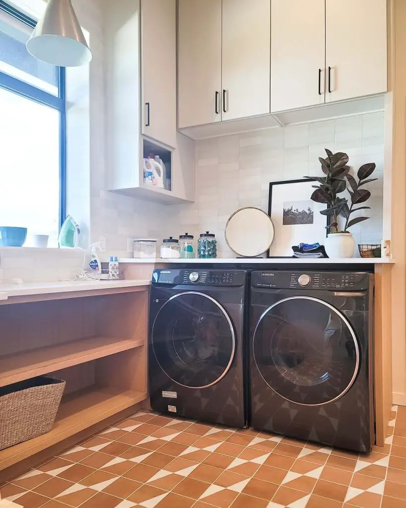 Modern laundry room with dark washers white cabinets and terracotta floor tiles