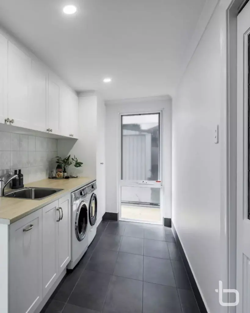 Long white laundry room with wooden countertop and dark floor
