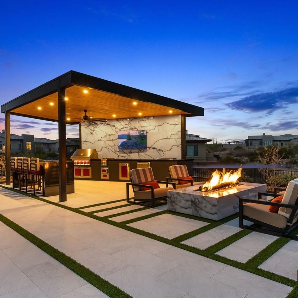 Modern outdoor kitchen and lounge area with firepit at twilight