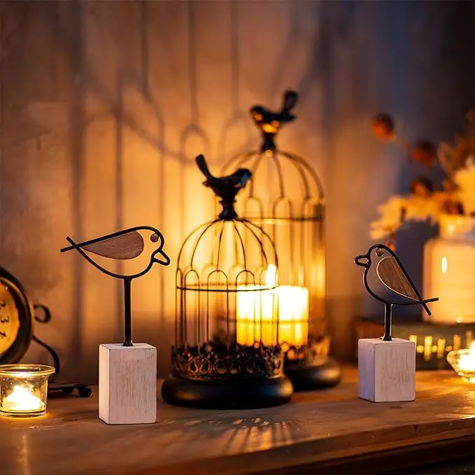 A cozy, warm-lit scene featuring decorative bird figurines perched on white blocks and black birdcages with candles inside.
