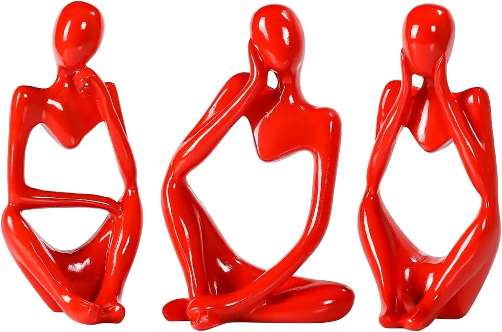 Three abstract, red resin sculptures depict seated figures in different contemplative poses