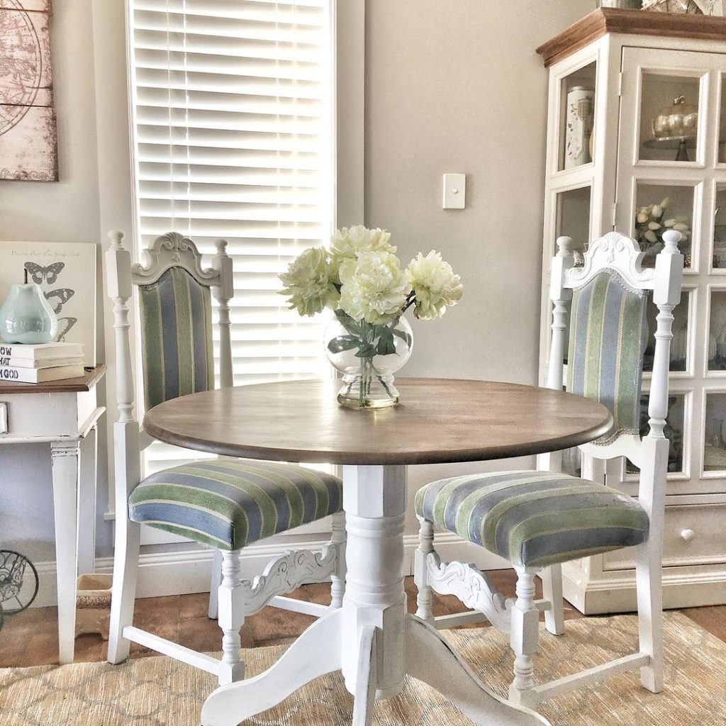 Vintage-style dining area with round table, striped chairs, and white flowers.
