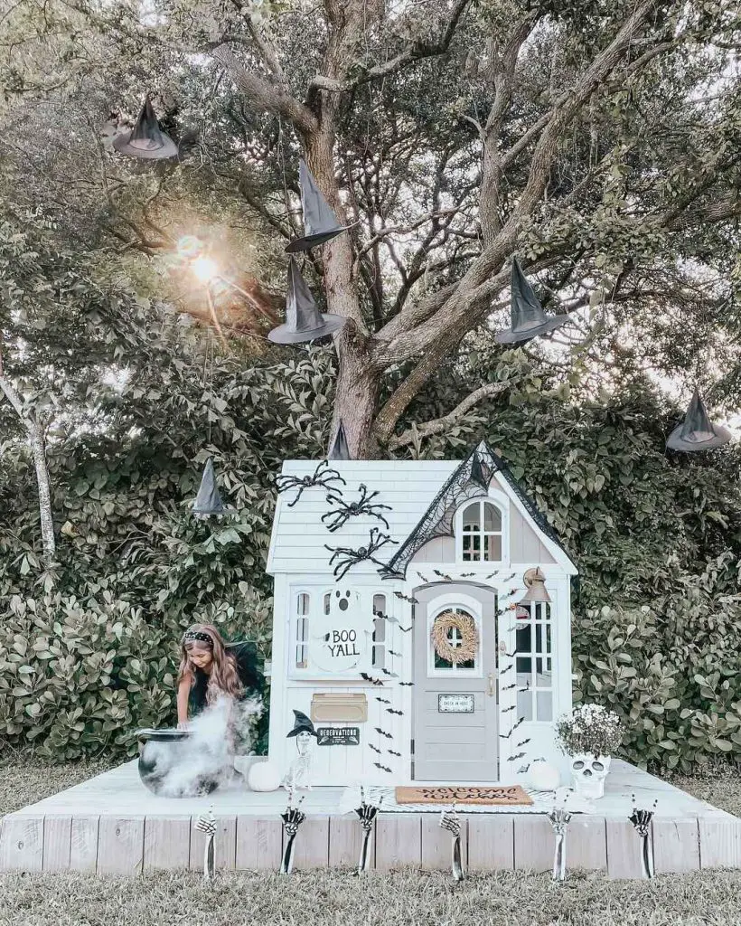 Playhouse decorated as witch cottage with hanging hats and child stirring cauldron