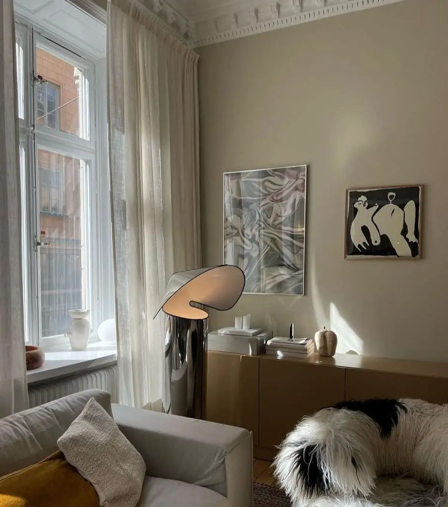  A minimalist living room with a neutral sofa, chrome floor lamp, contemporary artwork, and a wooden credenza. 