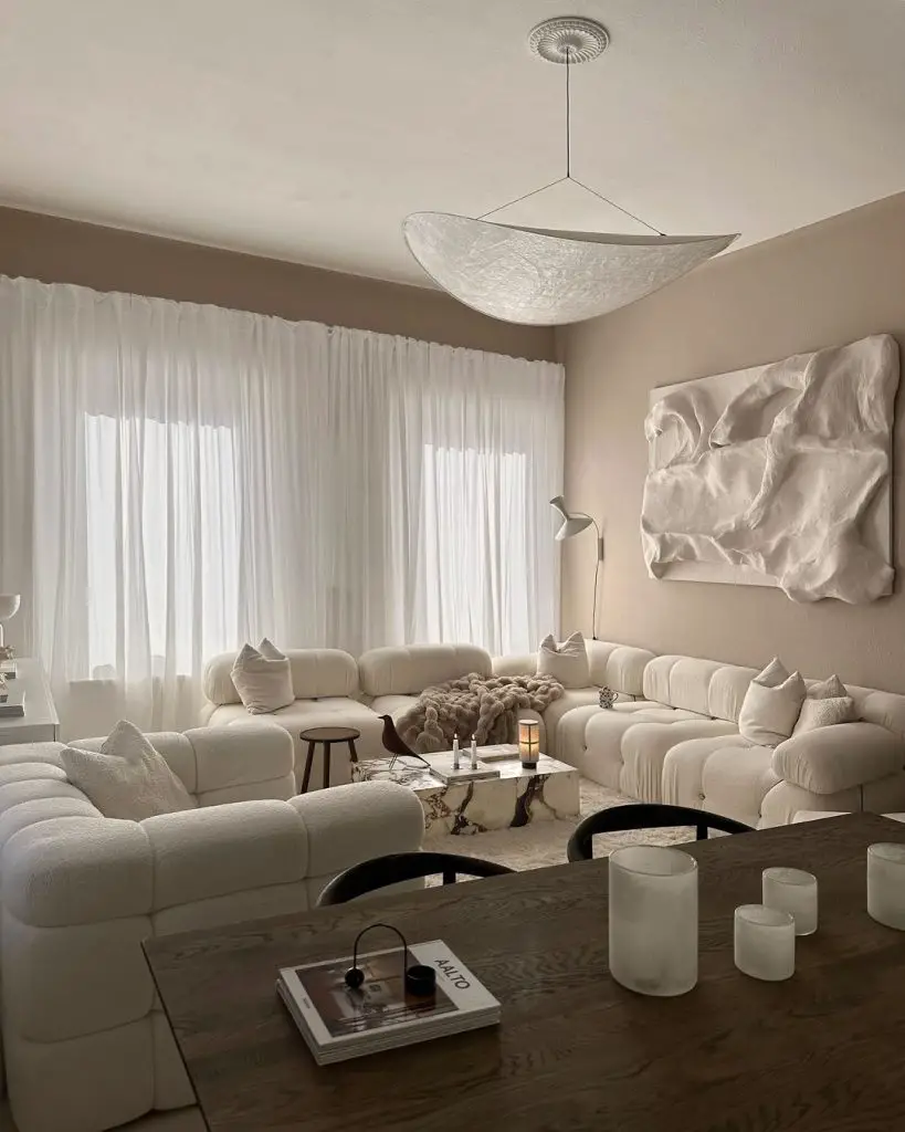 Minimalist white living room with cloud-like sofas and floating light fixture.