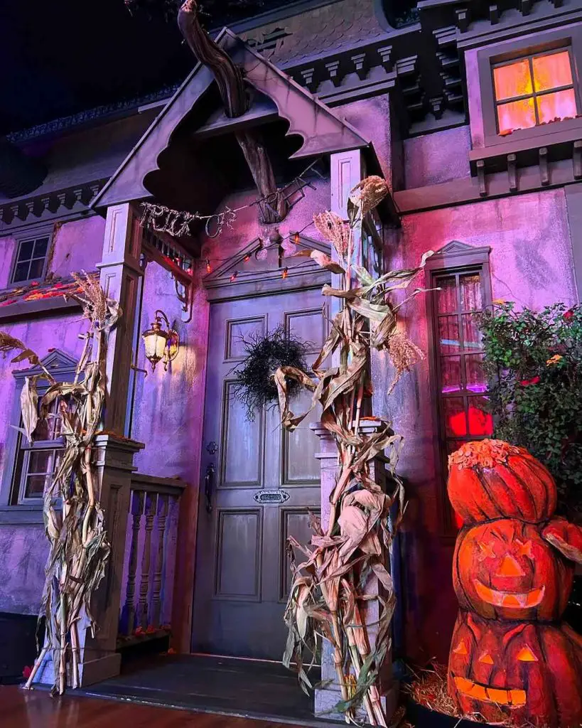 Purple-lit haunted house entrance with cornstalk decorations and glowing pumpkins.