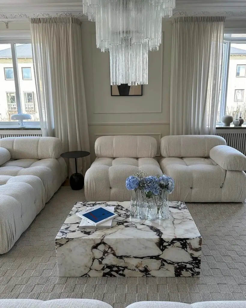 Luxurious white living room with plush sofas, large marble coffee table, and dramatic glass chandelier.