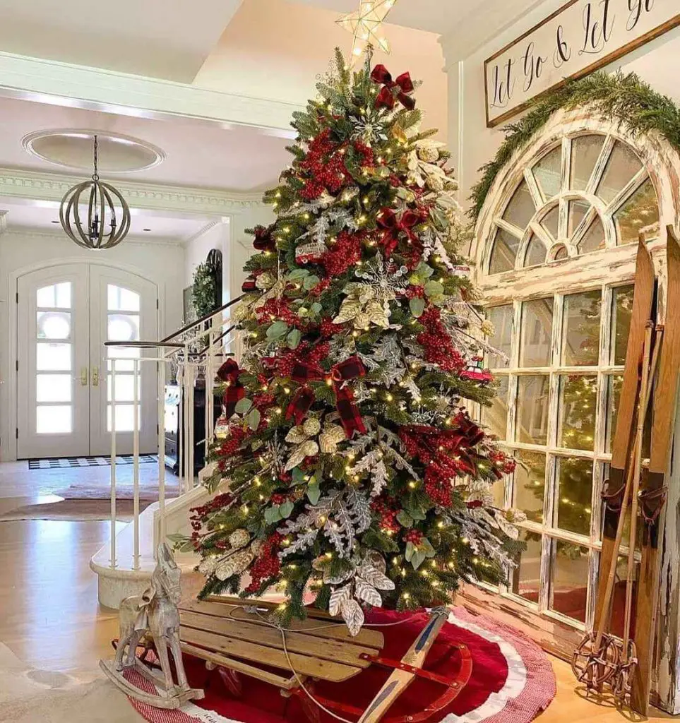 Elegant Christmas tree with red and silver decor atop vintage sleigh in bright farmhouse entryway