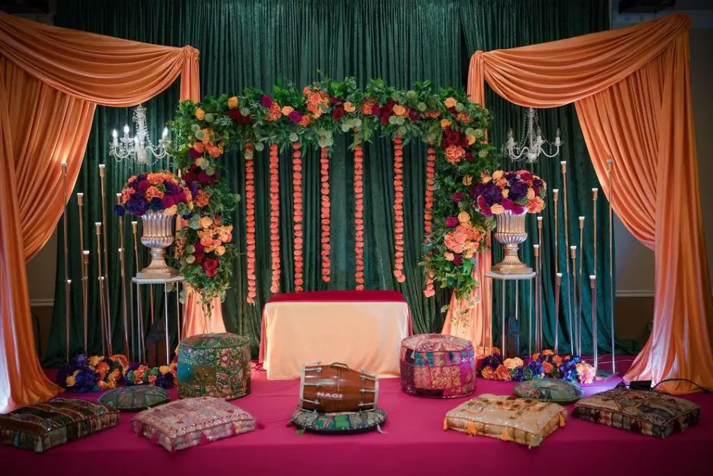 Wedding stage decorated with red tablecloth, patterned pillows and chandeliers.